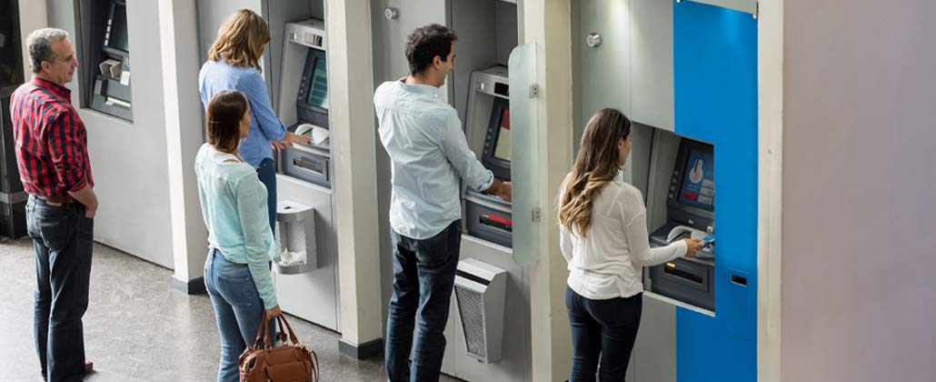 Pessoas em fila para levantar dinheiro em caixas multibanco, dentro de um banco